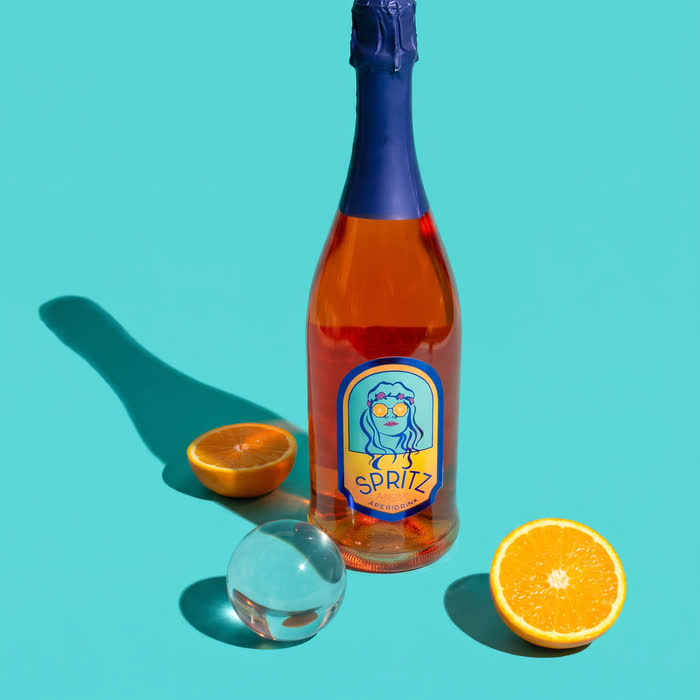 An aperitivo bottle on turquoise with an orange half and a glass sphere