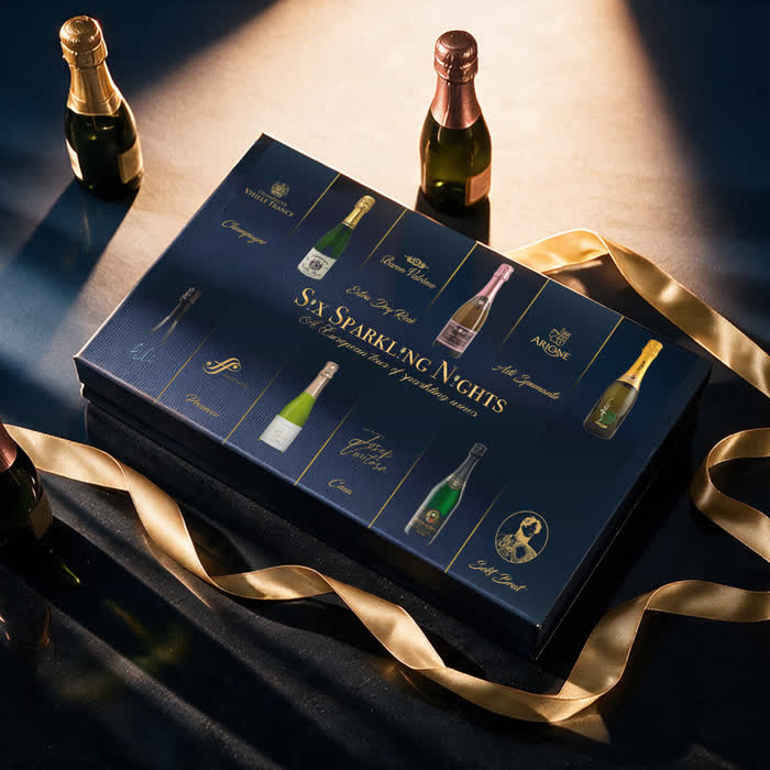 A navy gift box of six sparkling wines with a gold ribbon, lit low
