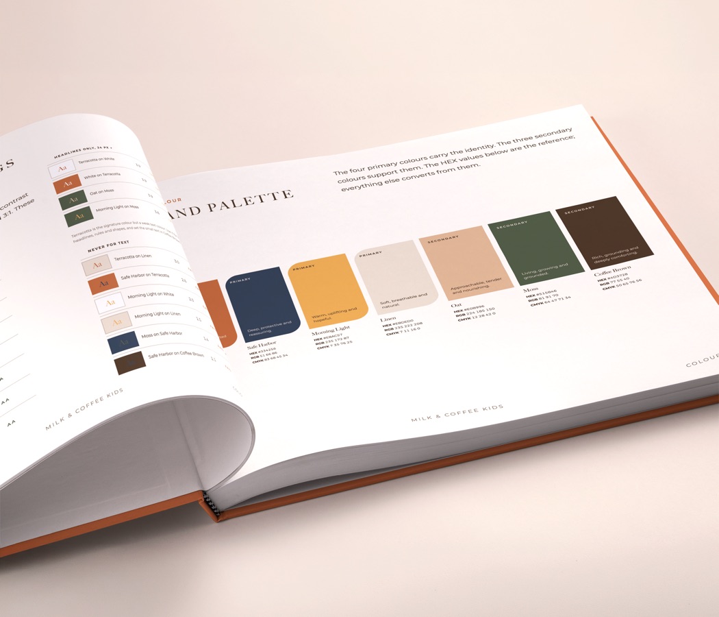 The printed brand guide open at the colour palette, each swatch with its values, and the pairing and contrast rules on the facing page