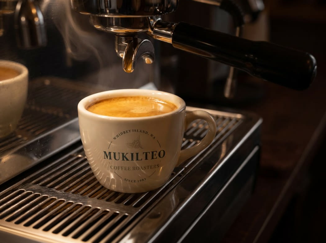 A branded ceramic cup standing whole on the drip tray beneath an espresso machine group head
