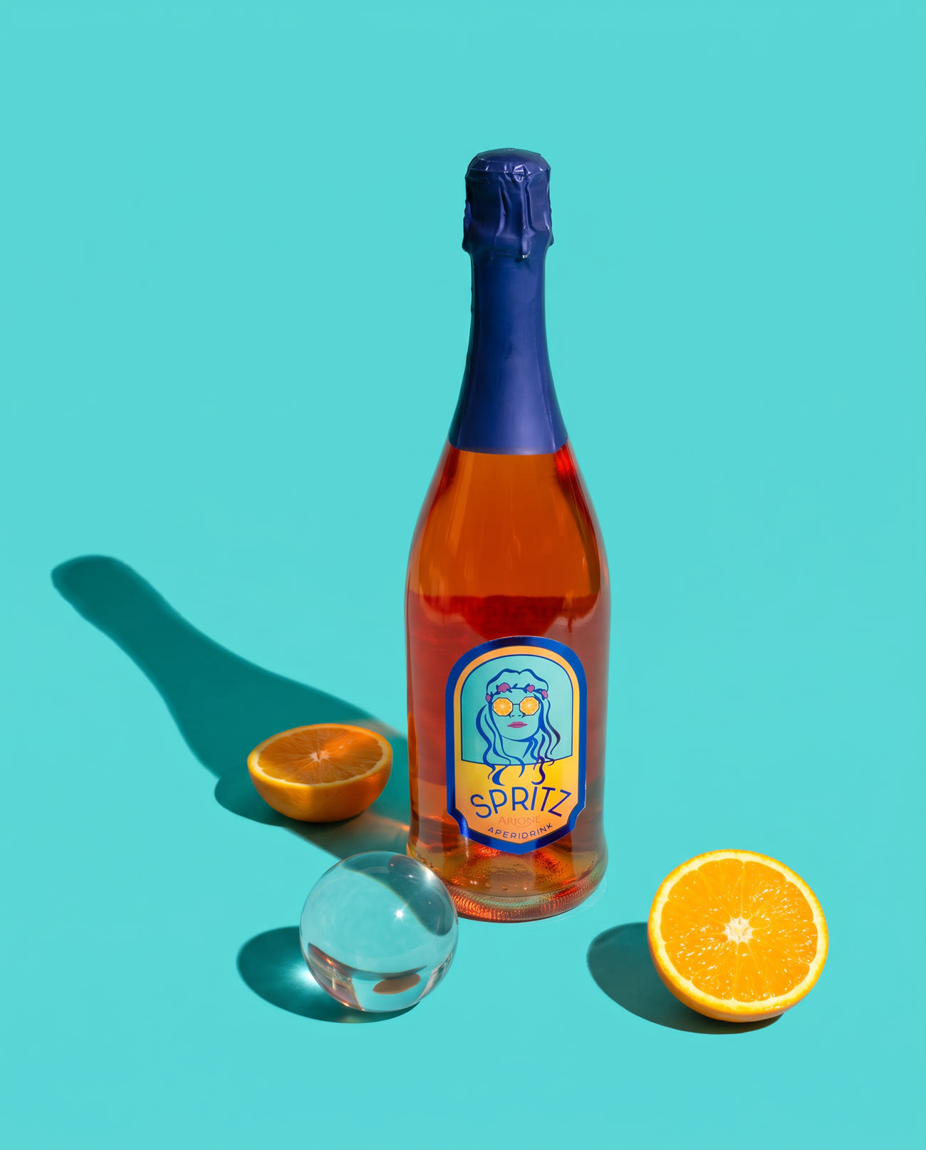 The Spritz bottle standing on a saturated turquoise ground with a hard cast shadow, cut oranges beside it